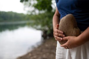 Frau mit einem Stein in den Händen am Wasser – Retreat für Frauen in Zeiten des Wandels